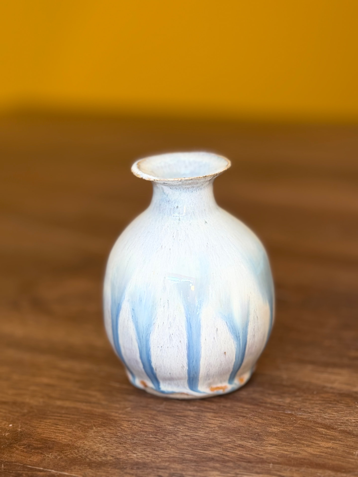A little bud vase with blue glaze drips on a wooden table