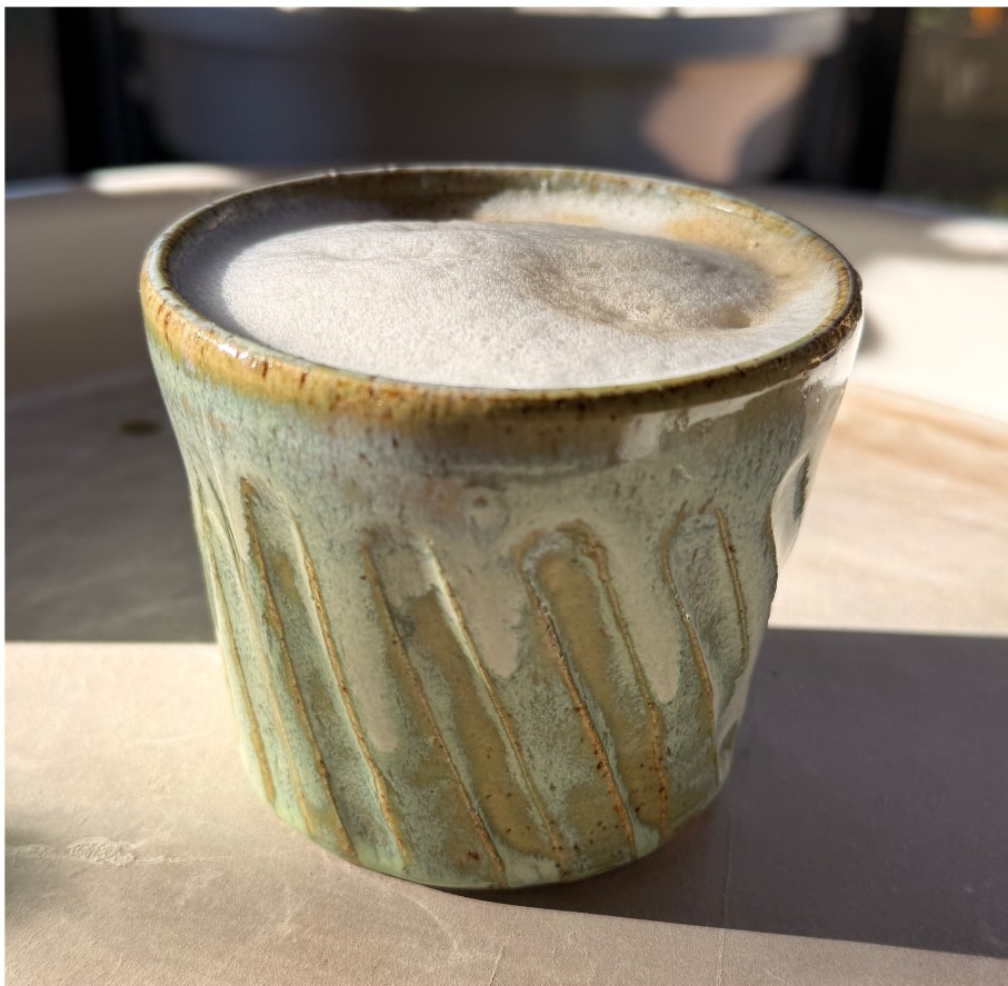 A green fluted cup with a foam-topped coffee, catching the afternoon sun