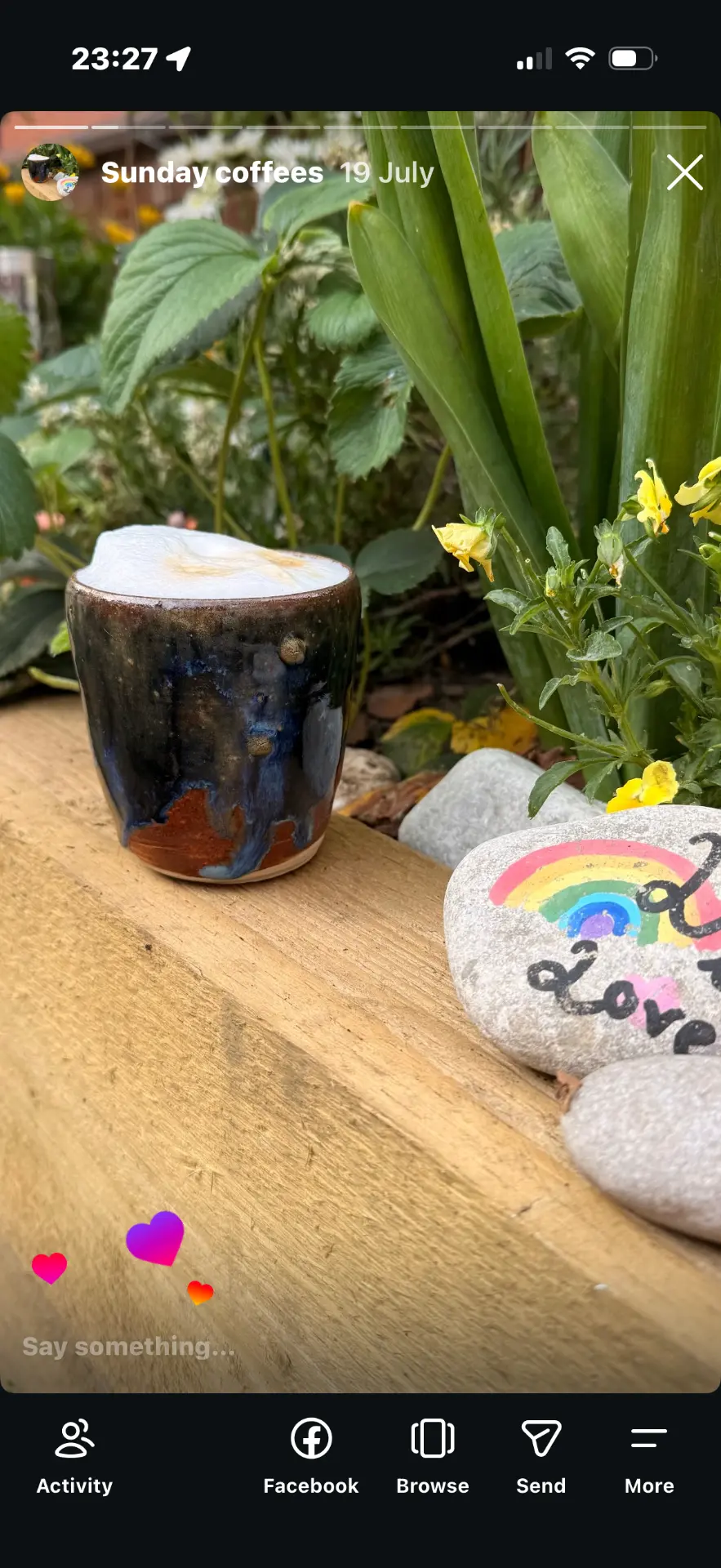 A deep blue handmade coffee cup nestled among flowers in the garden