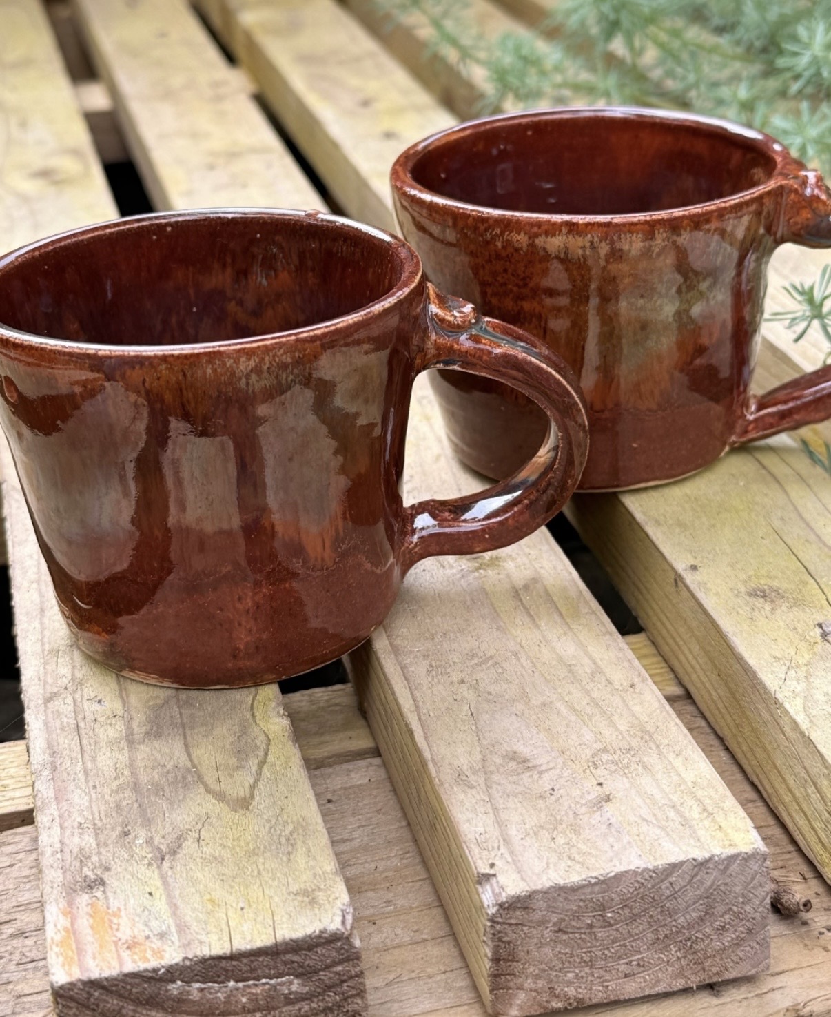 A pair of warm rust-glazed coffee cups on a wooden bench